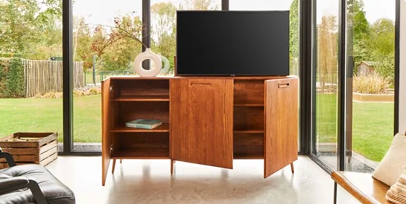 Mid-century modern kast met open deuren, tv erbovenop, in lichte kamer met glazen wanden en uitzicht op groene tuin.