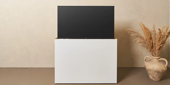 Strak wit tv-meubel met liftfunctie, geplaatst tegen een lichtbeige muur, naast een vaas met gedroogd pampasgras.