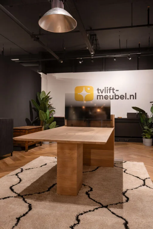 Moderne showroom met houten tafel op licht tapijt, omgeven door planten. Zwarte muren en industriële verlichting benadrukken de strakke stijl.